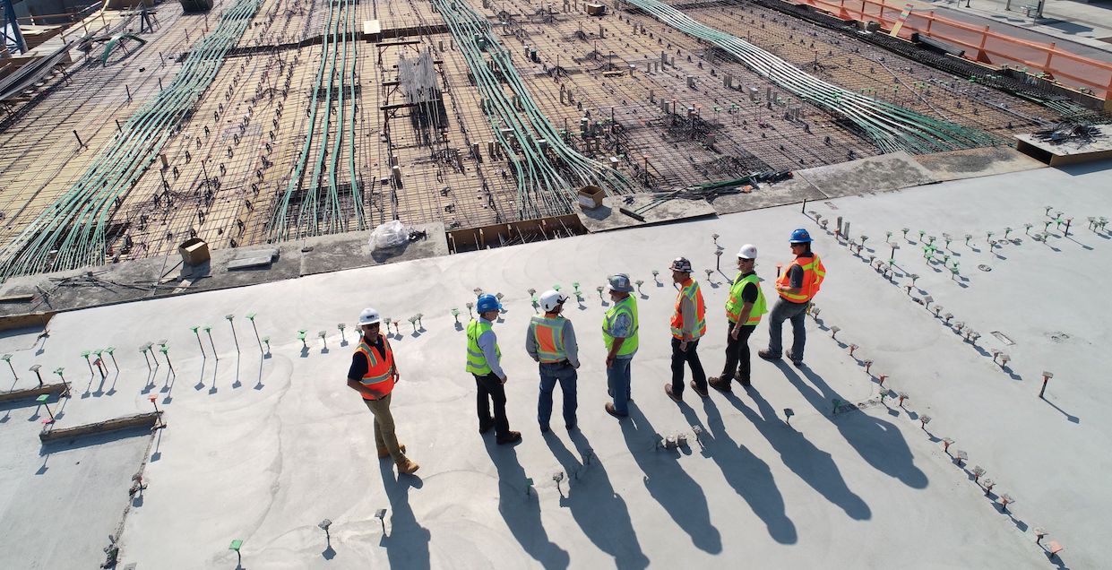 Photo of a building site with people standing on the foundations wearing high vis jackets and hard hats.