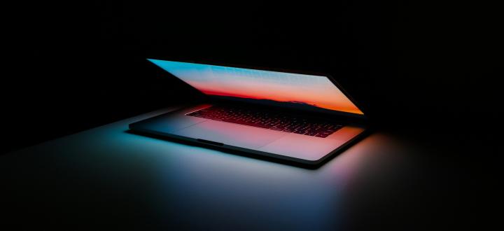 A photo of a laptop in a dark room slightly open, with a sunrise showing on the screen which reflects onto the keyboard