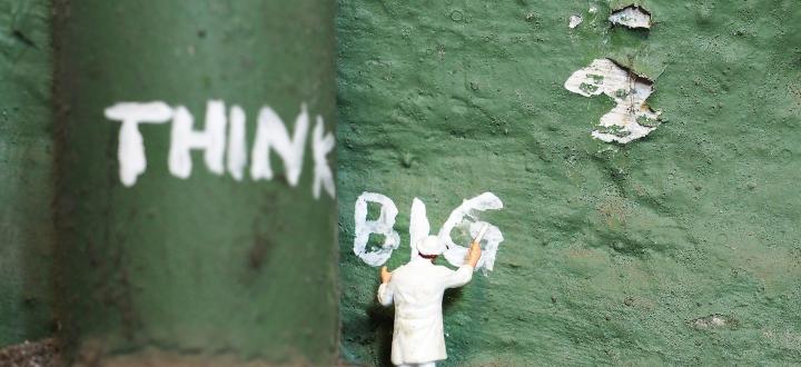 Photo of small figure painting 'think big' onto a green pipe and wall