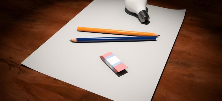 Photo of paper with two pencils, an eraser and a lightbulb on a wooden surface