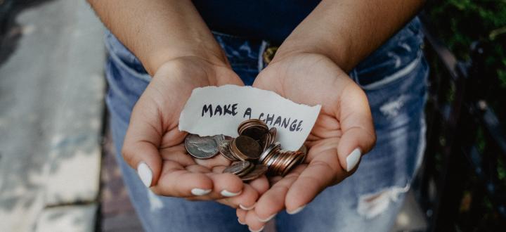 Photo of hands holding coins with a piece of paper which has 'make a change' written on it.