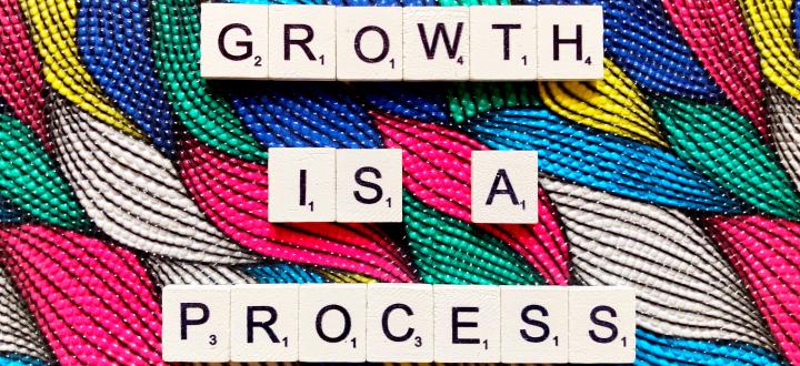 Photo of brightly coloured fabrics woven together with the words 'Growth is a process' in scrabble letters on top.