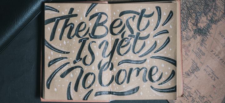 Photo of a drawing on two pages of a notebook which says 'the best is yet to come' with the pen beneath the notebook and another to the side.
