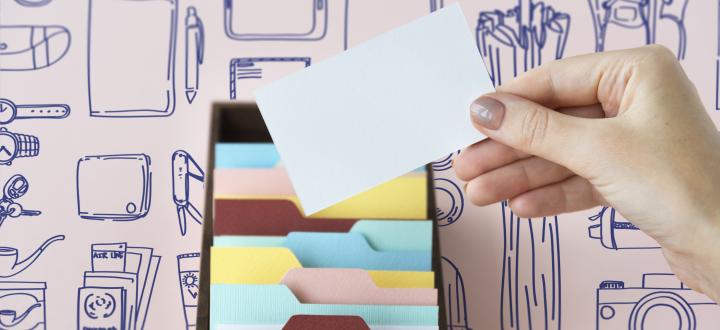 A photo of a woman holding a blank business card in front of a filing system. There's a background wallpaper of doodles which are tech equipment and office supplies.