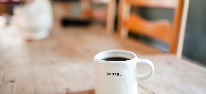 Photo of a white coffee mug on a table with the word 'begin' written on it