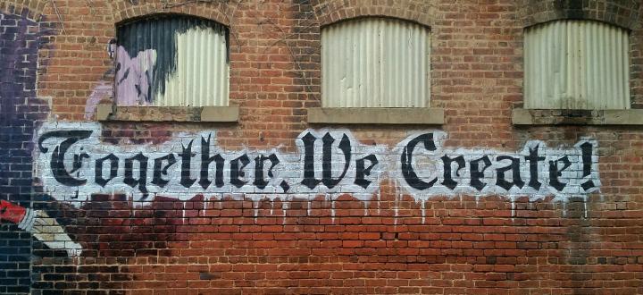 A wall with 'Together We Create' painted on it in gothic style lettering