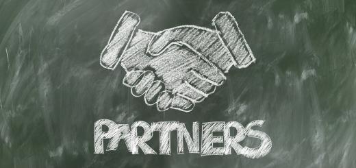 Illustration of two hands shaking in chalk on a blackboard with 'partners' written in block caps below.